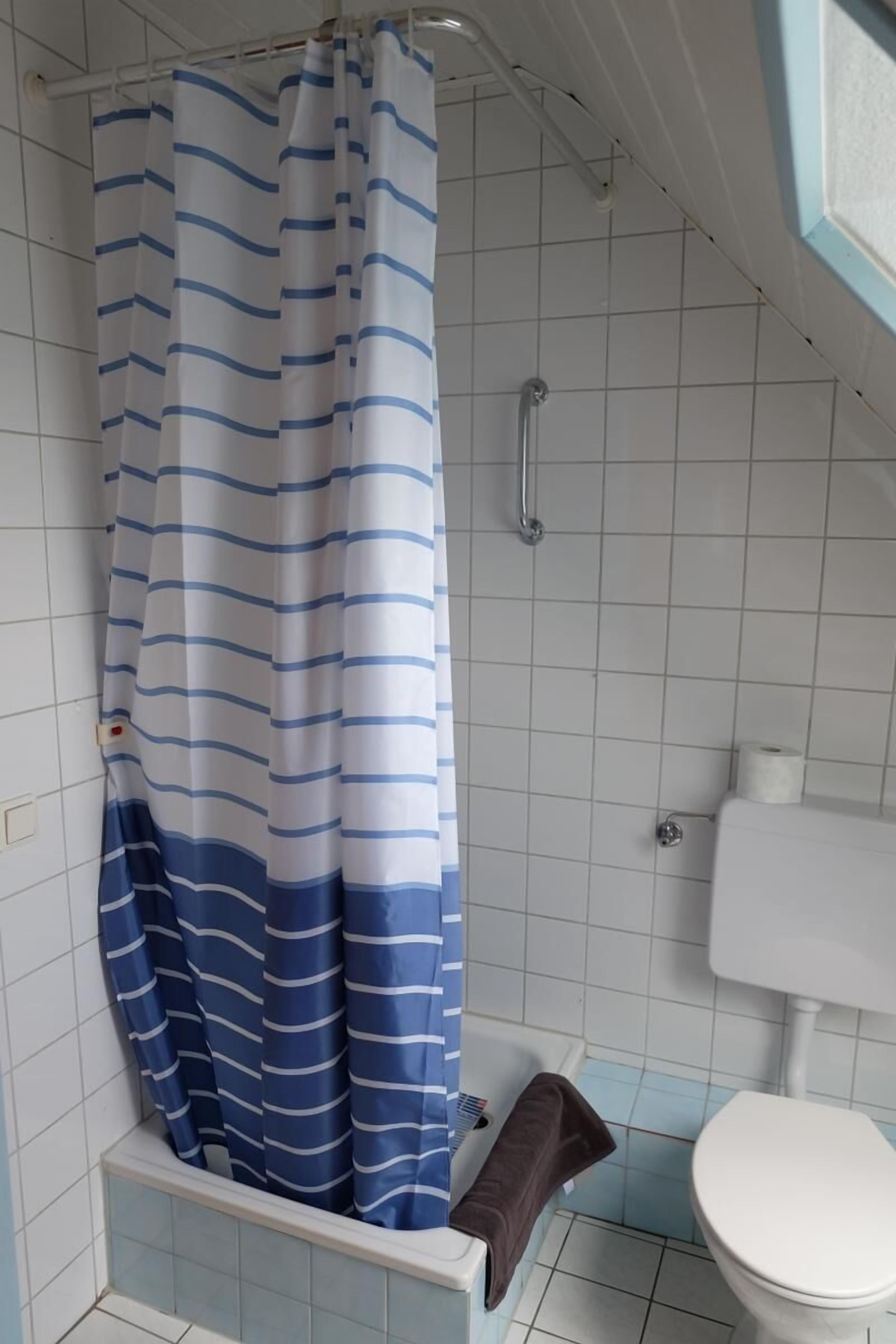 Een badkamer met douchegordijn, toilet en bad.