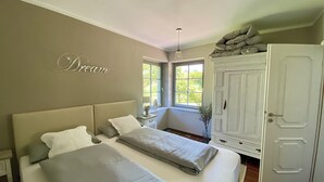 Une chambre avec deux lits, une armoire, une fenêtre donnant sur un beau paysage et un panneau décoratif sur le mur avec le mot « Rêve ».