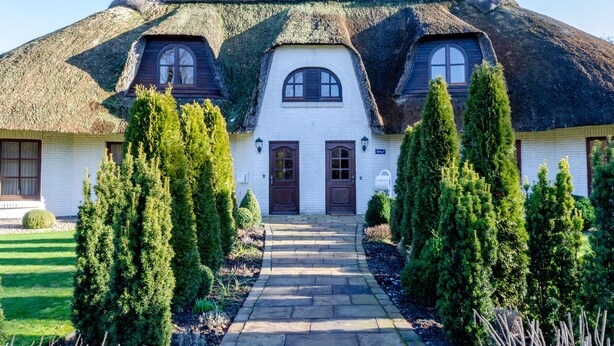 Une maison avec un toit de chaume, des murs blancs et une entrée centrale dotée de deux portes.