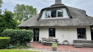 Une maison avec un toit de chaume, des murs extérieurs en briques blanches et un patio aménagé avec du mobilier d’extérieur.