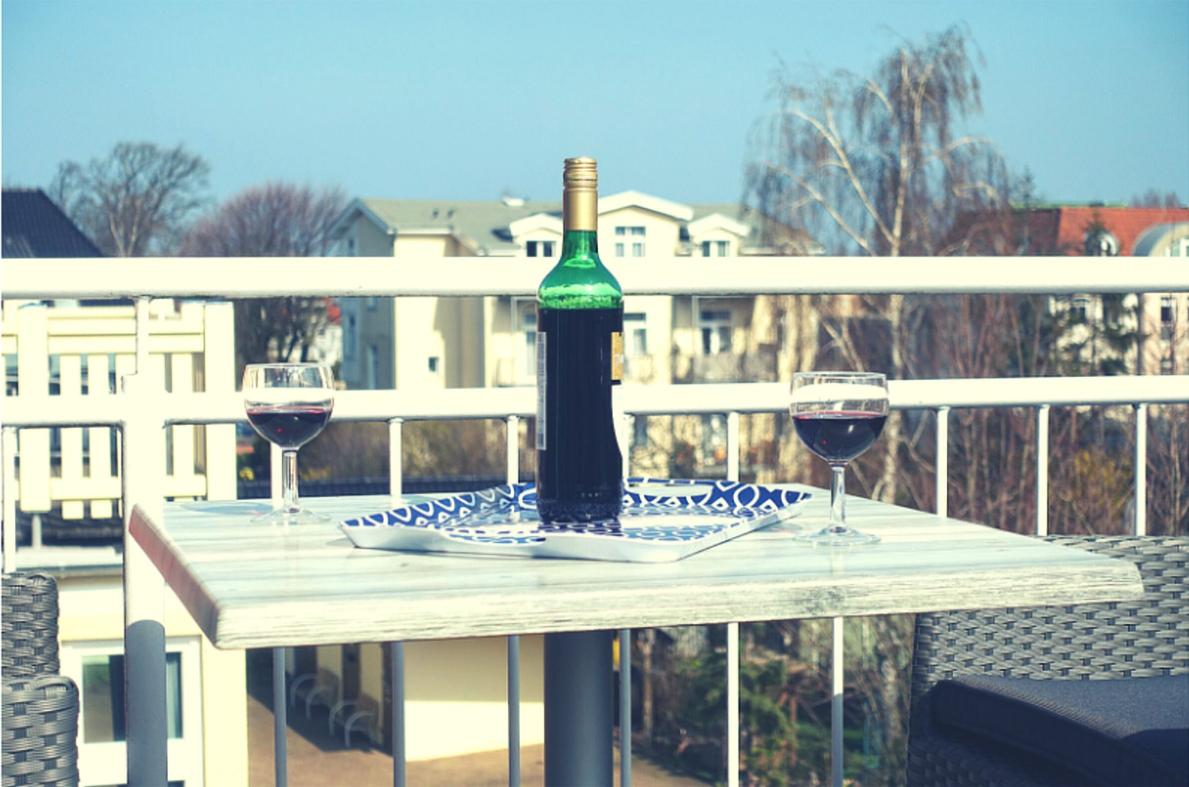 A balcony with a table set for two, featuring two wine glasses and a bottle of wine.