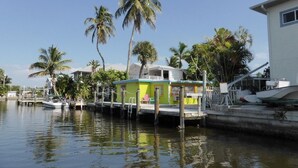 A houseboat docked at a marina with a small deck and a covered area, surrounded by palm trees and other vegetation. - Sun, beach, and great deals—discover dream vacation destinations with discounts (Matlacha)