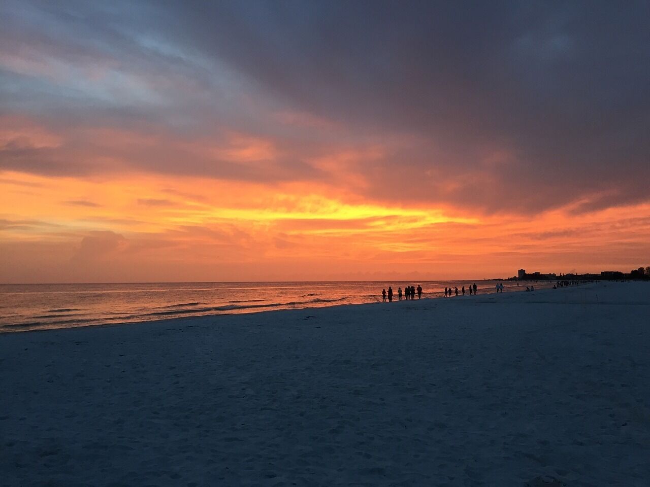 A beach with people walking along the shore during sunset.