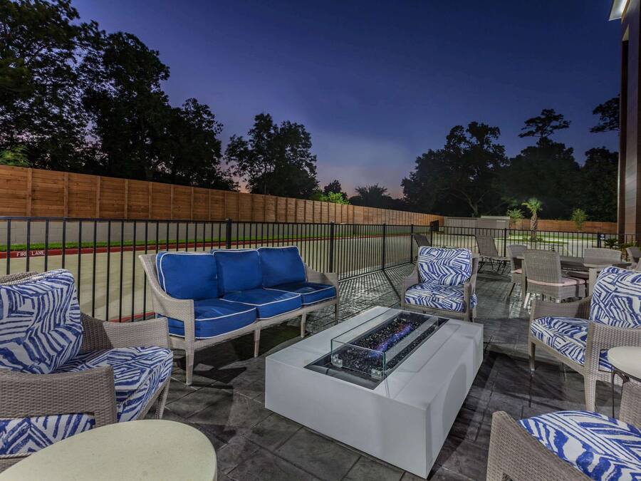 Un espacio patio al aire libre con mobiliario de mimbre, una mesa de centro de vidrio y vista a un edificio al fondo.