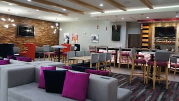 A modern lounge area with seating arrangements, a bar, and a television screen.
