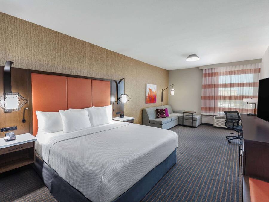 A hotel room with a large bed, a desk, a chair, a sofa, and a TV.
