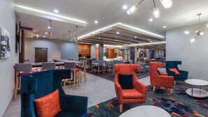 A modern hotel lobby with seating areas, a reception desk, and a library in the background.