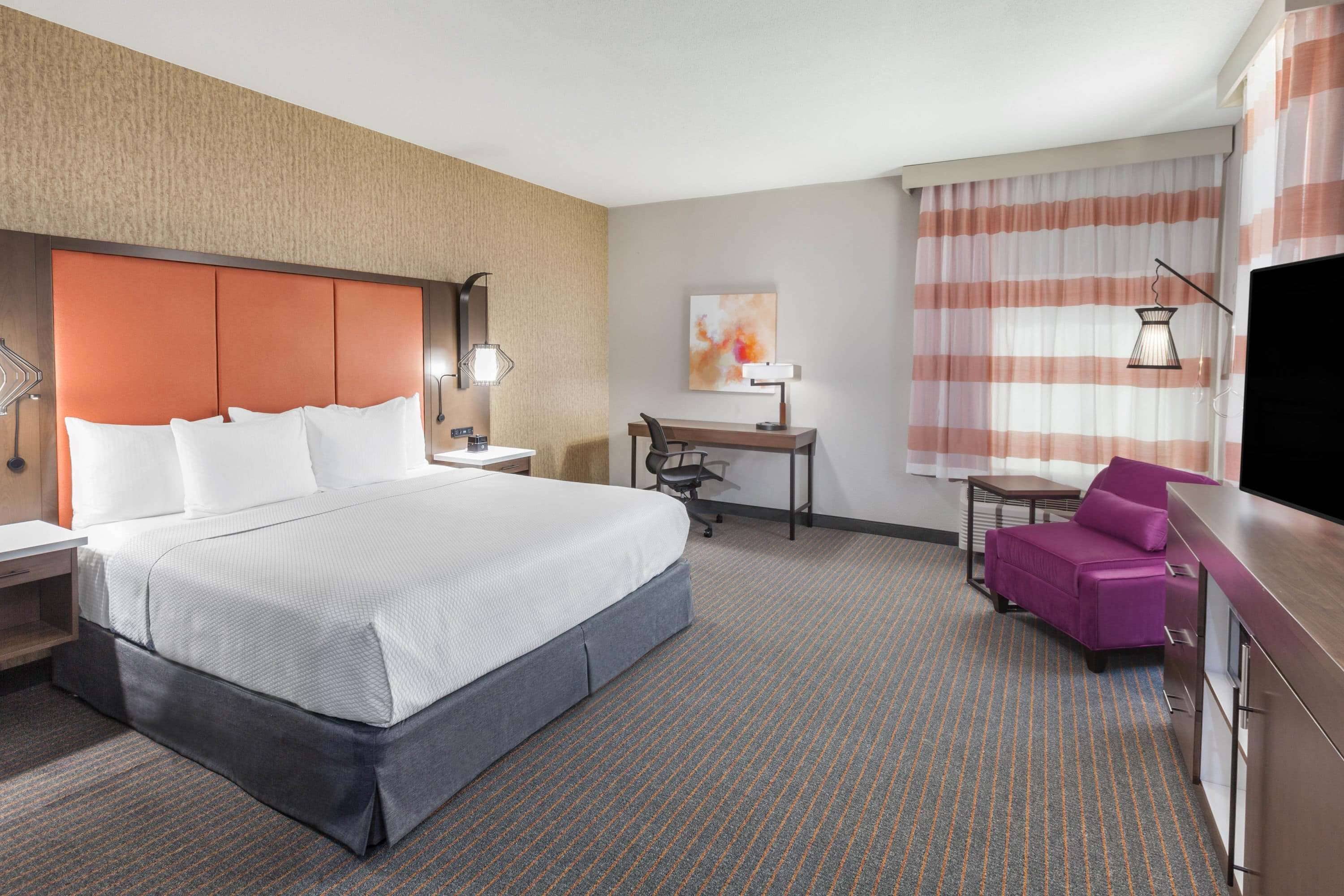 A hotel room with a large bed, a desk, a chair, and a TV.