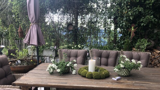 An outdoor patio with wicker furniture, a wooden table, and a candle centerpiece. - comfortable (Riefensberg)