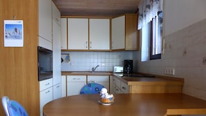 Eine kleine Küche mit Holzausstattung, einem Spülbecken, einem Toaster und einer Kaffeemaschine. Vorhanden ist ein runder Tisch mit einem Stuhl.