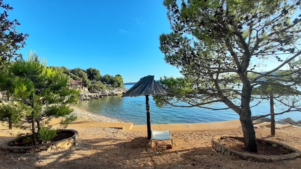 Ein Strand mit Sandfläche, einer kleinen weißen Bank und einem reetgedeckten Sonnenschirm.