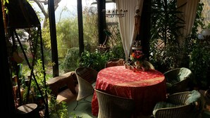 A cozy indoor garden with a round table covered in a red tablecloth, surrounded by wicker chairs. - Romantic Black Forest house, enchanted garden, half-timbered town of Schiltach  (Schiltach)