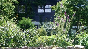 A stone wall with a garden in front of a house with a dark roof and windows. - Romantic Black Forest house, enchanted garden, half-timbered town of Schiltach  (Schiltach)