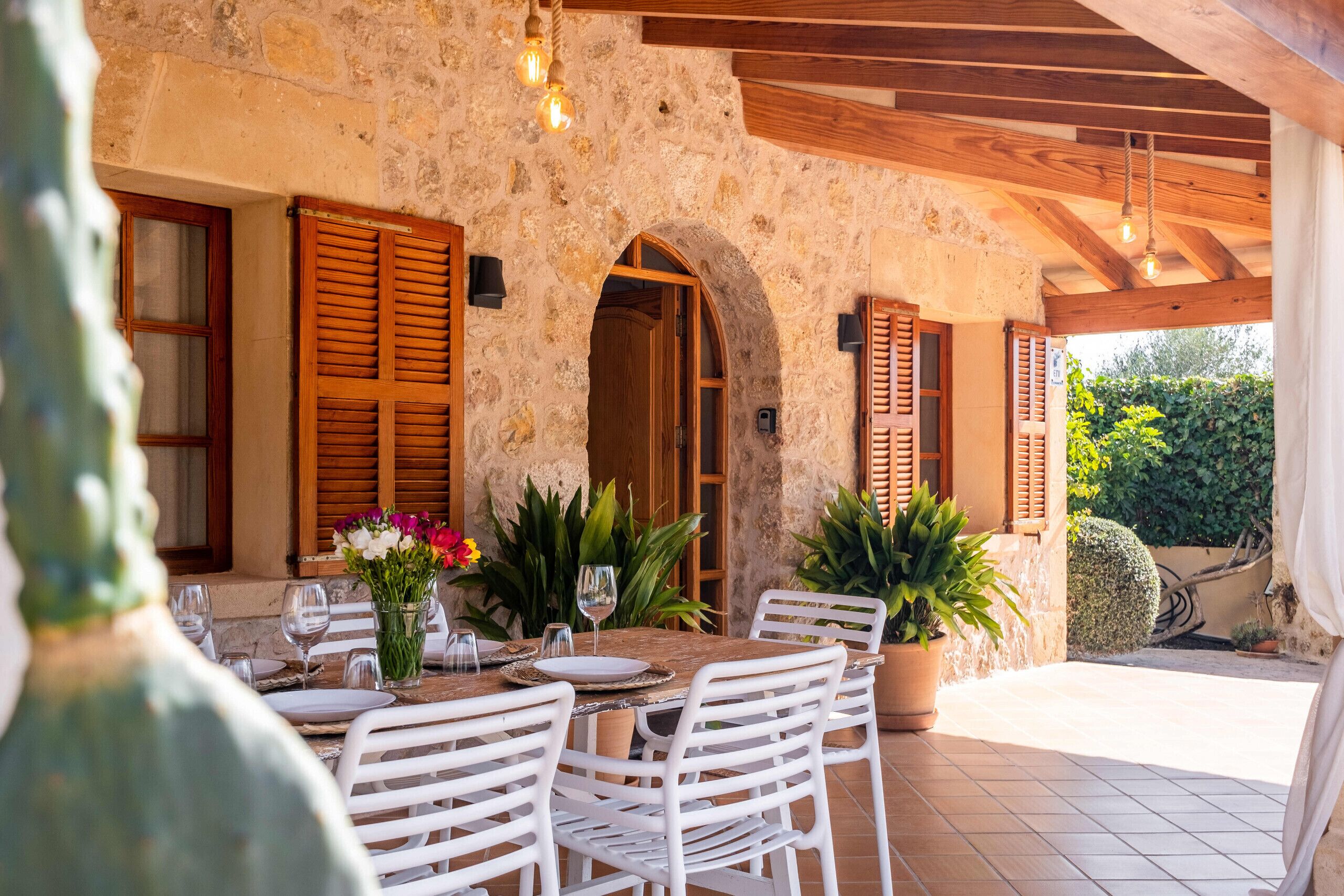 A stone building with wooden shutters, a table set for dining, and potted plants.