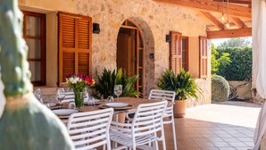 A stone building with wooden shutters, a table set for dining, and potted plants. - Villa with pool  Pollensa - Can Roig Guillem (Pollensa / Pollença)