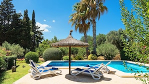 A pool area with lounge chairs and a thatched umbrella, surrounded by greenery and trees. - Villa with pool  Pollensa - Can Roig Guillem (Pollensa / Pollença)