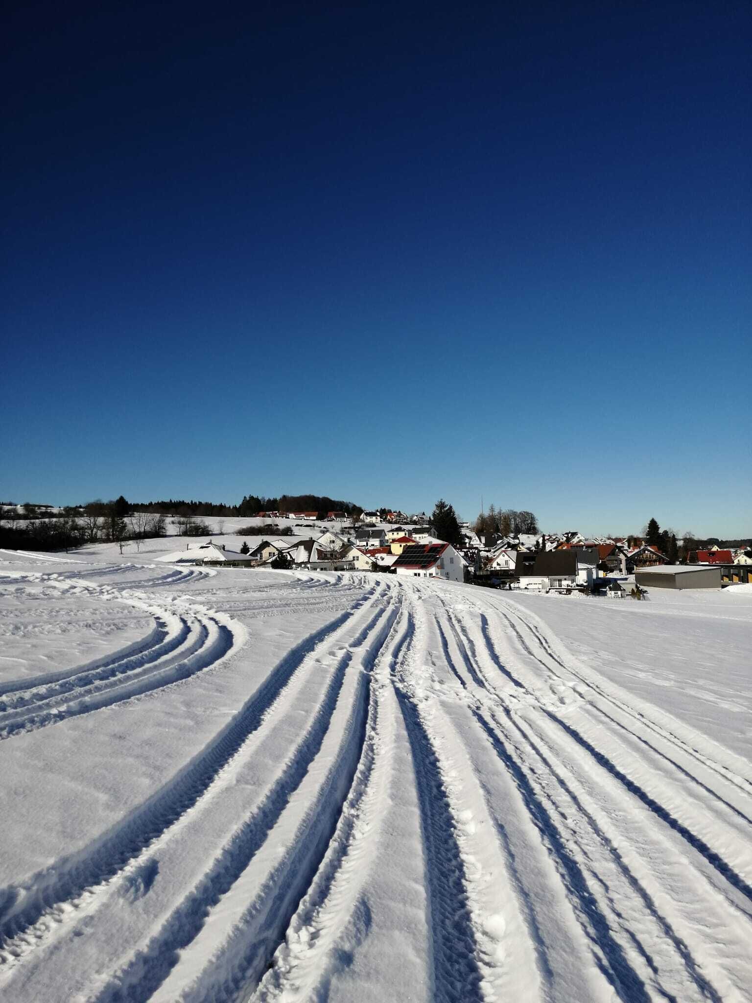 A snowy landscape with tracks leading to a cluster of buildings.