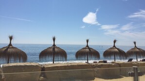 A beach with thatched umbrellas and a clear blue sky.