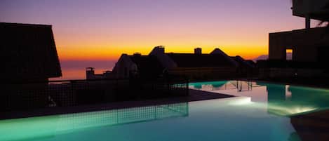 A pool area with a sunset view, overhanging roofs, and a calm water surface.