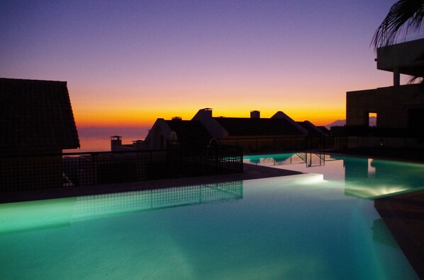 A pool area with a sunset view, overhanging roofs, and a calm water surface.