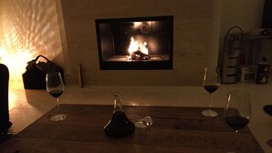 A cozy room with a fireplace, a wooden table with wine glasses and a decanter, and a wall-mounted TV.