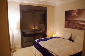 A hotel room with a bed, a sliding door closet, a lamp, and a painting on the wall.