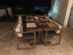 An outdoor dining area with a wooden table and chairs, a candle, and a view of the city at night.