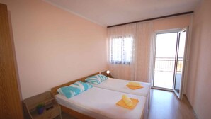 Una habitación pequeña y limpia con dos camas individuales, una mesita de noche y una ventana con cortinas.