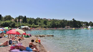 Una playa con gente tomando el sol, nadando y jugando. Hay sombrillas y sillas de playa.