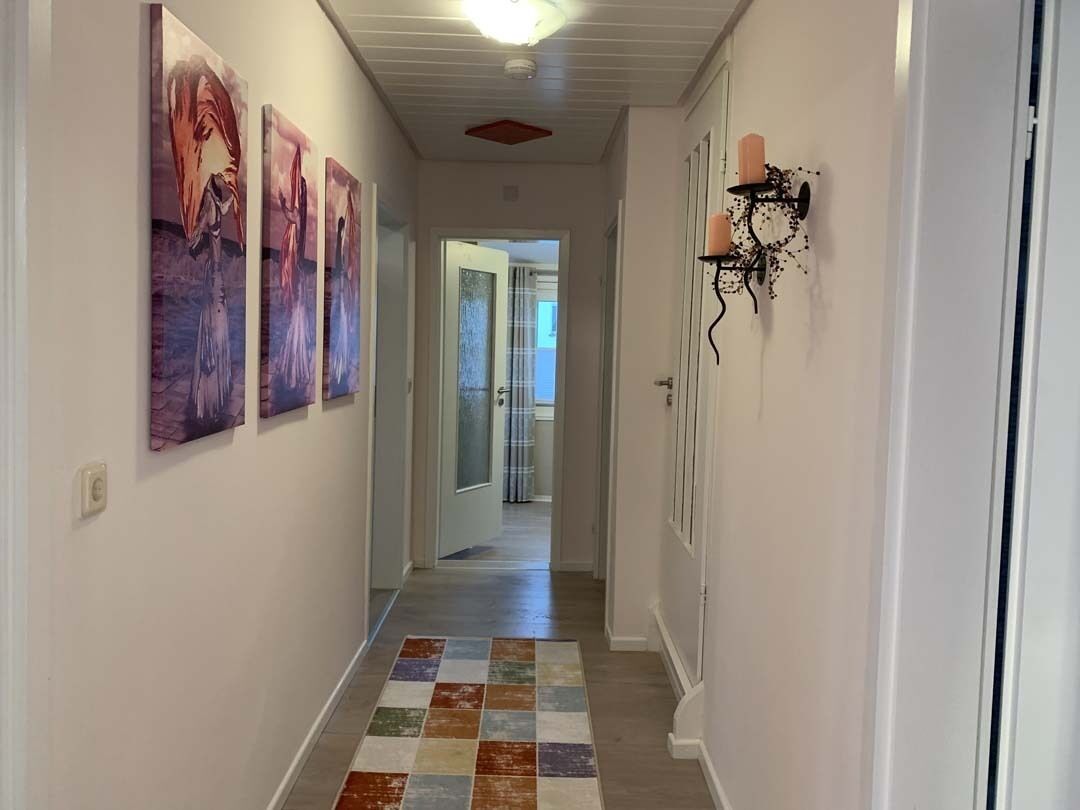 A hallway with a colorful rug, a wall-mounted light fixture, and a door leading to another room.