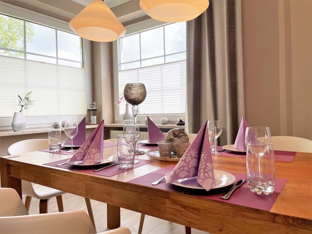 A dining table set with purple napkins, plates, and glasses, with a vase of flowers and a decorative bowl on the table.