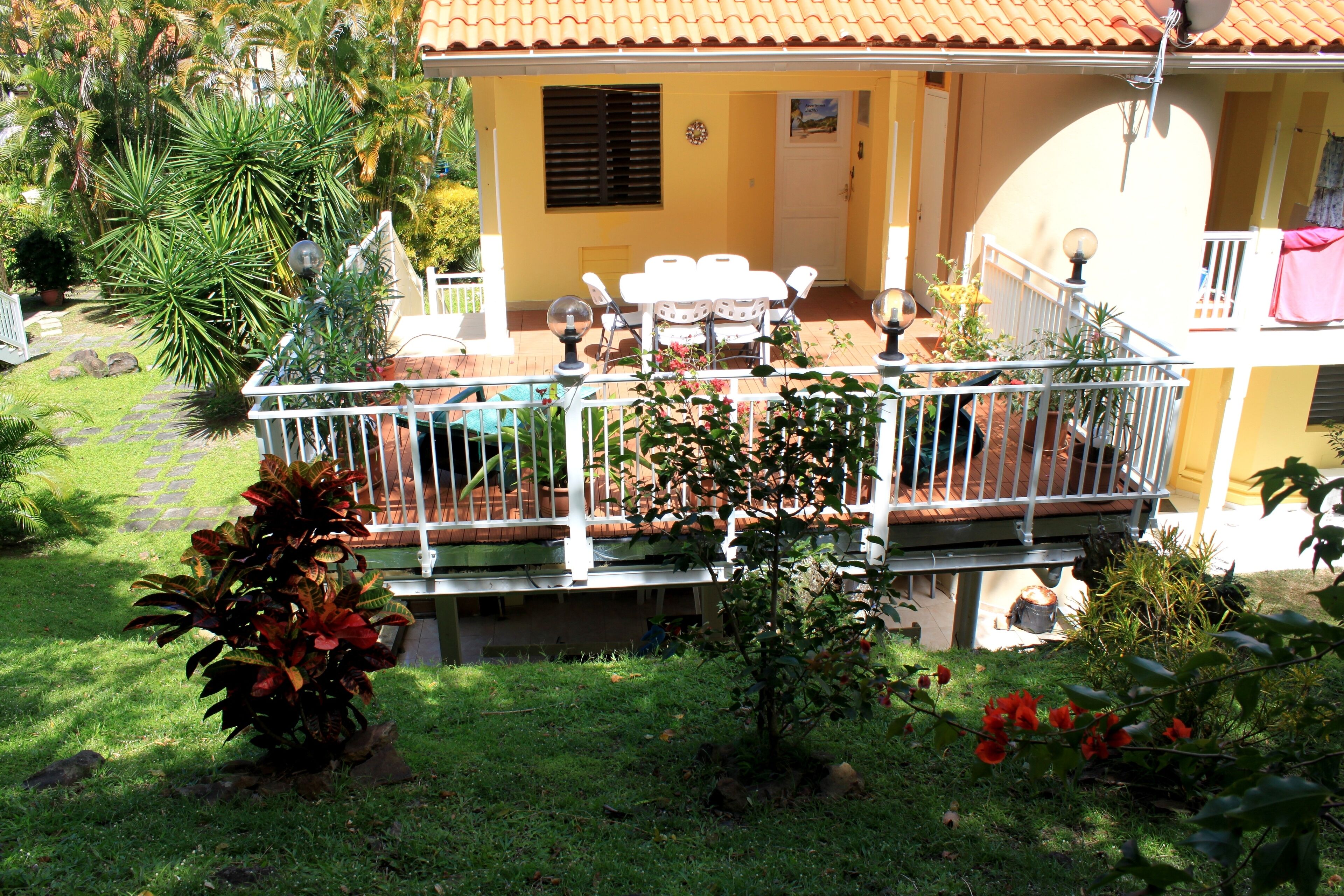 Uma casa de dois andares com varanda, um pátio com mobiliário de exterior e um jardim com diversas plantas.