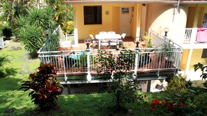 A two-story house with a balcony, a patio with outdoor furniture, and a garden with various plants. - Nice apartment in a quiet resort with pool only 50m from the beach. (Trois-Îlets)