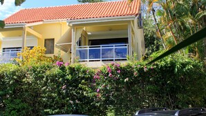 A two-story house with a red-tiled roof, a balcony, and a covered porch. - Nice apartment in a quiet resort with pool only 50m from the beach. (Trois-Îlets)