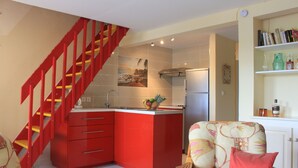 A modern kitchen with red cabinetry, a built-in island, and a red staircase. - Nice apartment in a quiet resort with pool only 50m from the beach. (Trois-Îlets)