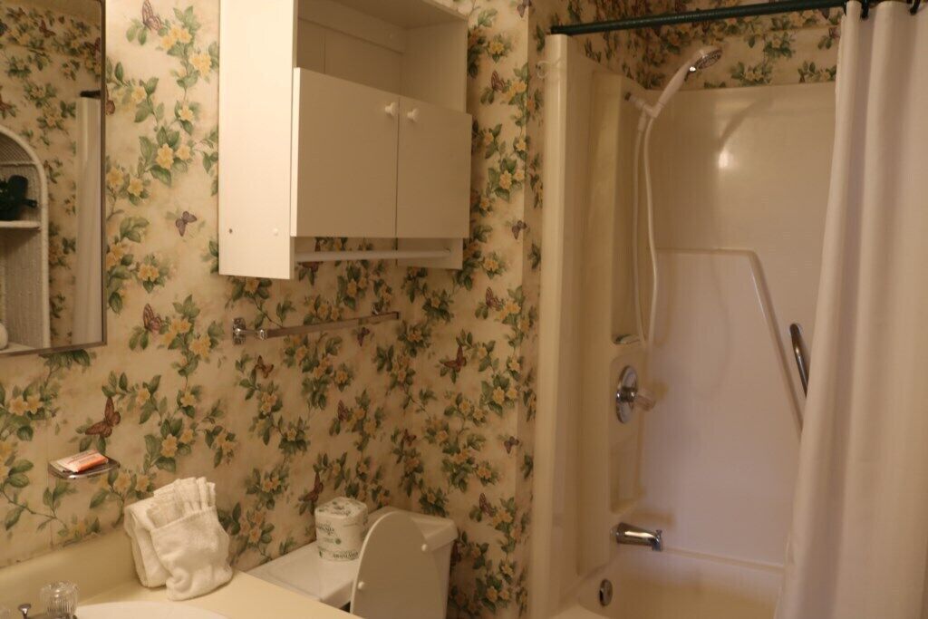 A bathroom with floral wallpaper, a toilet, a sink with a towel, and a shower area.