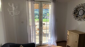 A room with a dark blue sofa, a wooden cabinet, and a view of a garden through a glass door.