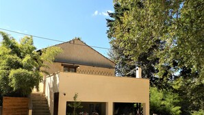 A two-story house with a staircase leading to the entrance, a small porch area with potted plants, and a fenced yard. - Gîte for 5 to 7 people in Sarlat. Heated swimming pool. Wifi. >>Nature (SARLAT LA CANEDA)