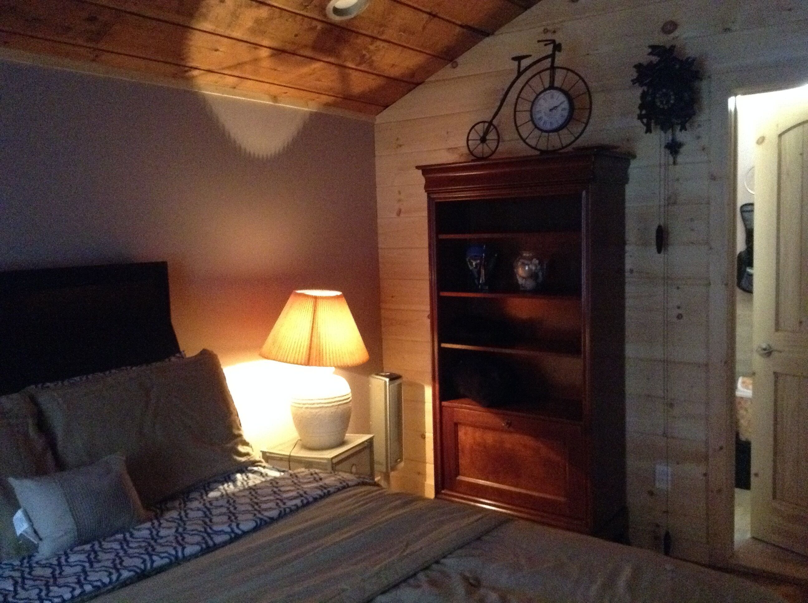 A bedroom with a bed, a bedside lamp, a wooden cabinet, and a wall-mounted bicycle clock.
