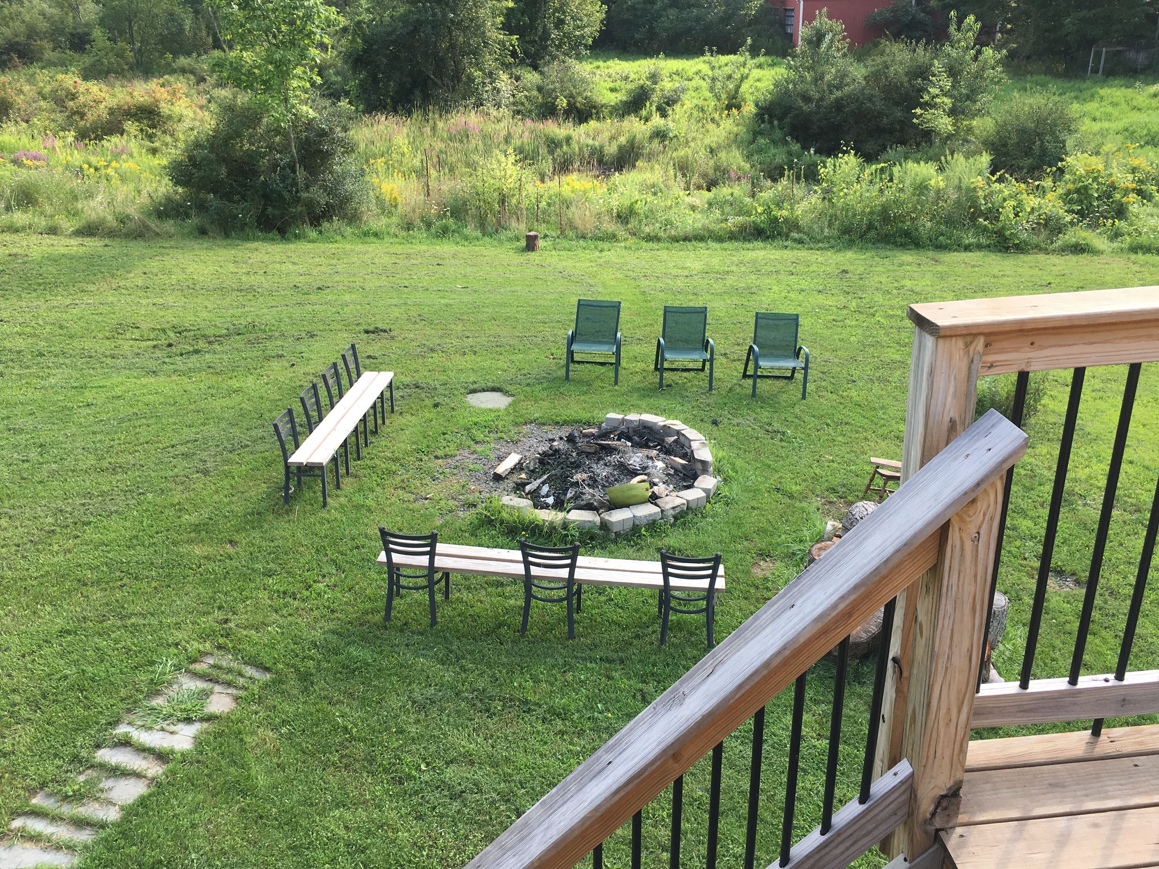 Ein Garten mit Rasenfläche, einem Feuerkorb, Sitzgelegenheiten im Freien und einer Holzterrasse.