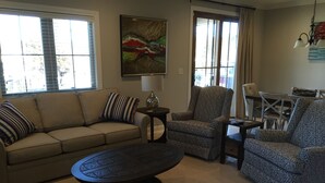 Ein Wohnzimmer mit einem beigen Sofa, gemusterten Sesseln, einem Couchtisch und einem Essbereich mit Tisch und Stühlen.