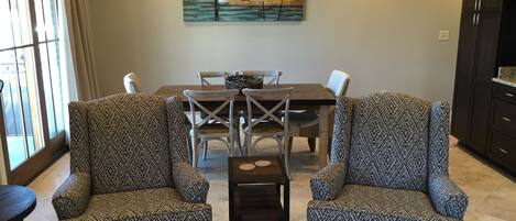 A dining area with patterned armchairs, a wooden dining table, and a painting above.