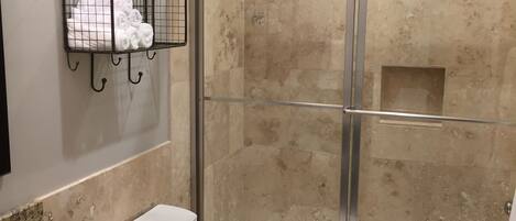 A bathroom with a granite countertop, a white toilet, a glass-enclosed shower, and a towel rack with towels.