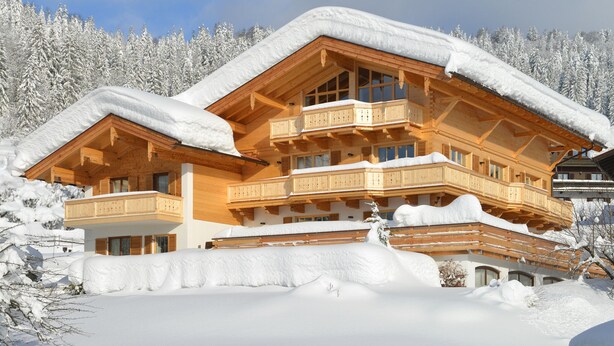 Ein mehrstöckiges Holzchalet mit Balkonen, umgeben von schneebedeckten Bäumen.