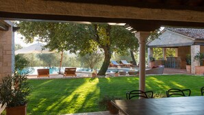 A covered patio area with a pool, outdoor seating, and a stone building in the background. - First class luxury villa with big pool, 1000sqm living area, 30000 sqm garden (porec)
