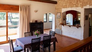 A dining area with a table set for six, a wooden ceiling, stone walls, and a view through a window.