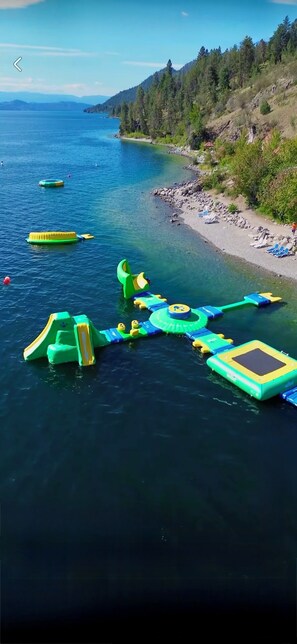 Un lac avec des structures de jeux flottantes et une plage équipée de chaises longues.