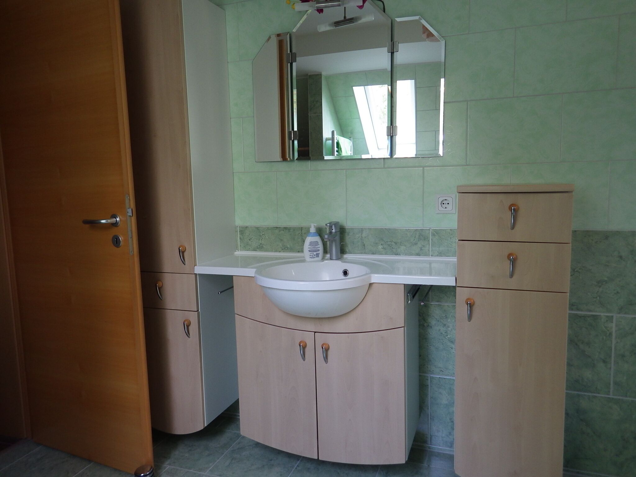 Een badkamer met een wastafel, spiegel en houten kastjes.