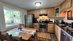 A kitchen with wooden cabinets, stainless steel appliances, a dining table with chairs, and a window with a view of trees. - 'Nob Nest' - Perfect location, Close to Everything (Sugar Mountain)