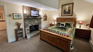 A bedroom with a stone fireplace, a bed with a green and red quilt, and a television mounted above the fireplace. - 'Nob Nest' - Perfect location, Close to Everything (Sugar Mountain)
